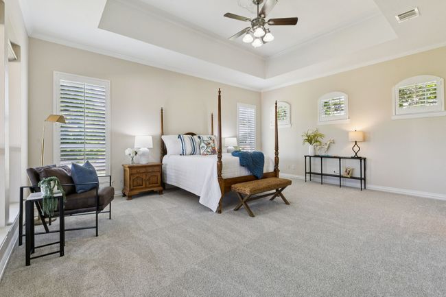 The spacious primary bedroom is separated from the rest of the house by a long hallway creating a peaceful oasis. To add to the relaxation of the room, there is space for a sitting area and a spa-like en suite bath. Other features include tray ceiling, plantation shutters, newly installed carpet, large 14 ft x 11 ft walk in closet with built-ins and ceiling fan. | Image 15