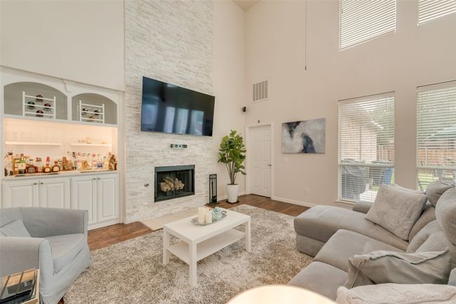 Living area featuring a high ceiling, wood finished floors, a stone fireplace, and baseboards | Image 9