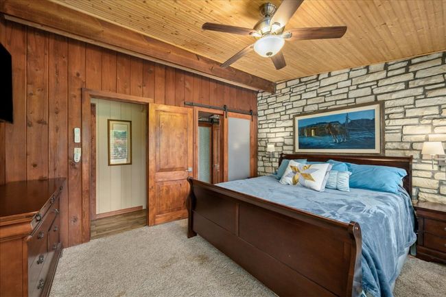 Bedroom featuring a barn door, a wood ceiling with exposed beams, carpet, wooden walls, and ceiling fan | Image 19