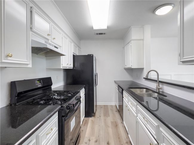 Kitchen with black gas stove, under cabinet range hood, dishwasher, light wood-style flooring, and white cabinetry | Image 6