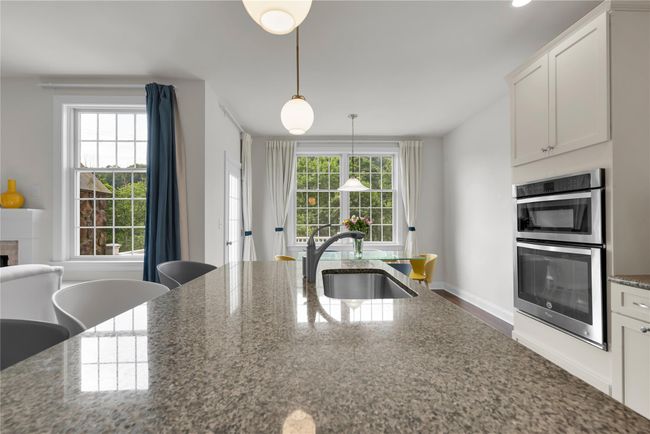 Kitchen with double oven, hanging light fixtures, white cabinetry, stone countertops | Image 6