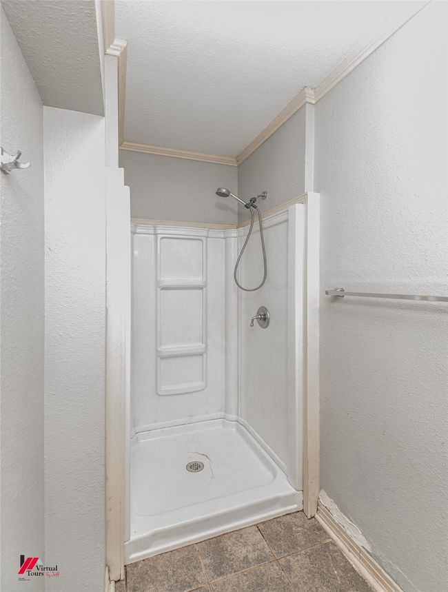 Bathroom featuring a textured ceiling, a shower, baseboards, ornamental molding, and a textured wall | Image 20