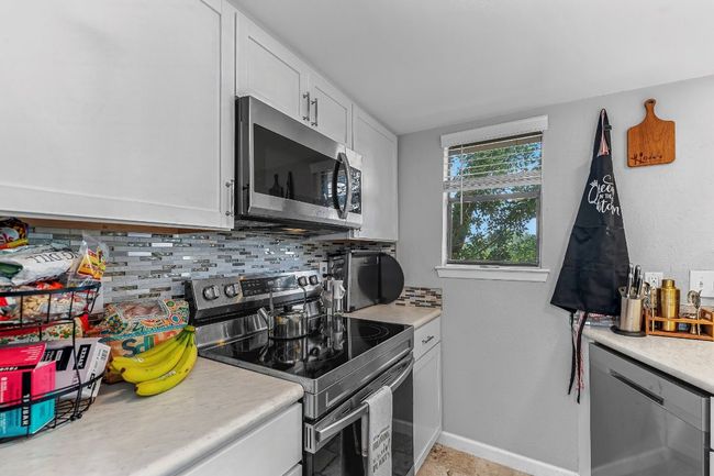 Kitchen with stainless steel appliances, decorative backsplash, light countertops, baseboards, and white cabinetry | Image 9