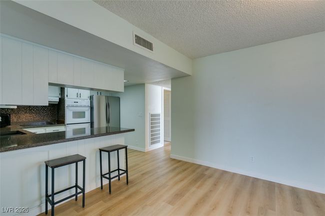 Kitchen featuring freestanding refrigerator, light wood-style floors, a breakfast bar area, a peninsula, and a textured ceiling | Image 20