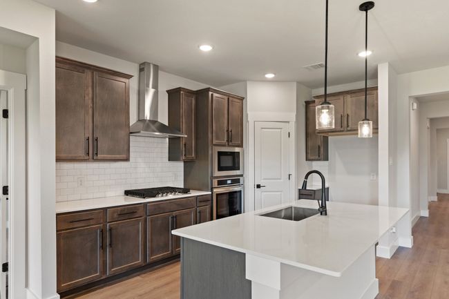 Kitchen featuring wall chimney range hood, appliances with stainless steel finishes, light wood finished floors, backsplash, and dark brown cabinetry | Image 6