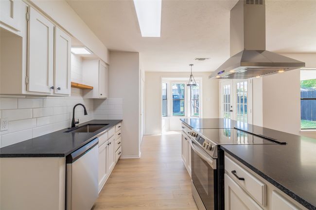 Kitchen with island exhaust hood, a sink, stainless steel electric range oven, dark countertops, and dishwashing machine | Image 9