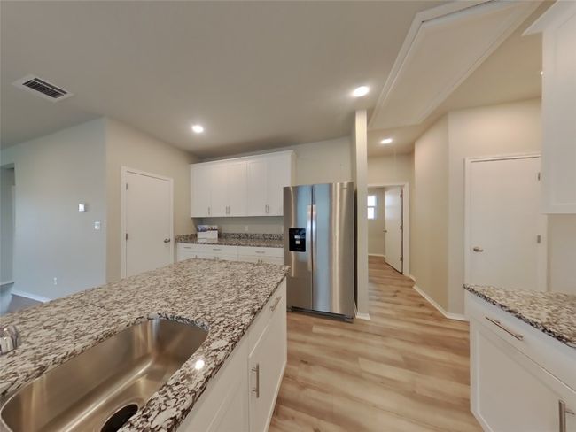 Kitchen featuring stainless steel refrigerator with ice dispenser, a sink, light wood finished floors, white cabinets, and light stone counters | Image 5
