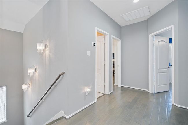 This photo shows a modern hallway with sleek hardwood floors and neutral gray walls. It features elegant wall sconces along a staircase, and multiple doorways leading to different rooms, enhancing the home's spaciousness and accessibility. | Image 16