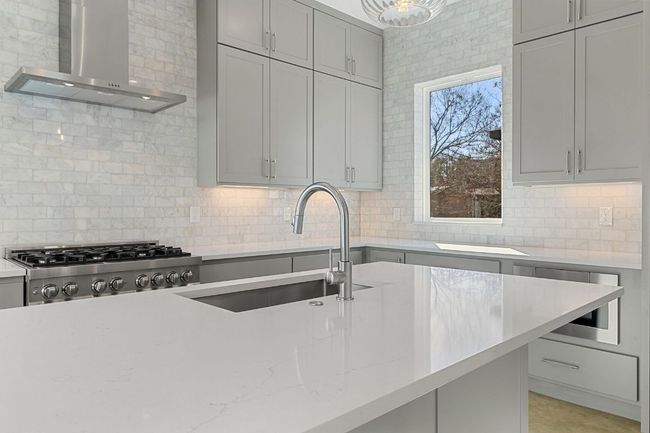 Kitchen with Marble backsplash, light stone countertops, gray cabinetry, wall chimney range hood, and a sink | Image 12