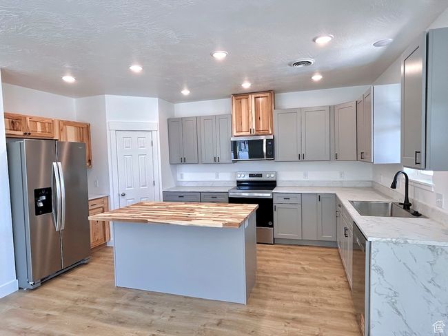 Kitchen featuring gray cabinets, stainless steel appliances, a kitchen island, wooden counters, and a sink | Image 33
