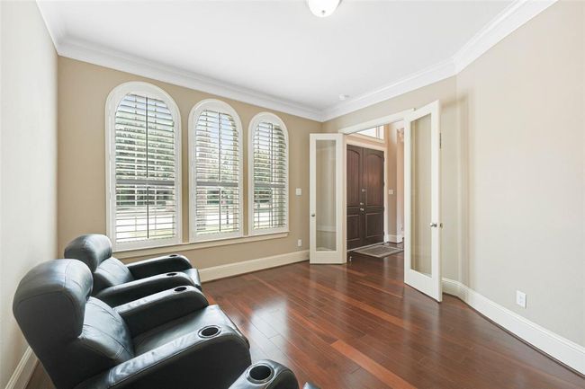 Flexible front room with elegant arched windows, French doors, and hardwood flooring—perfect for a home office, study, or media space. Plantation shutters add charm and natural light control. | Image 6