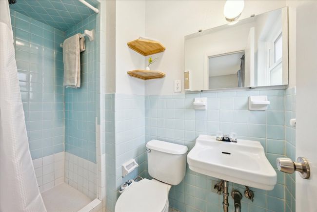 Full bathroom with toilet, wainscoting, a stall shower, tile walls, and a sink | Image 17
