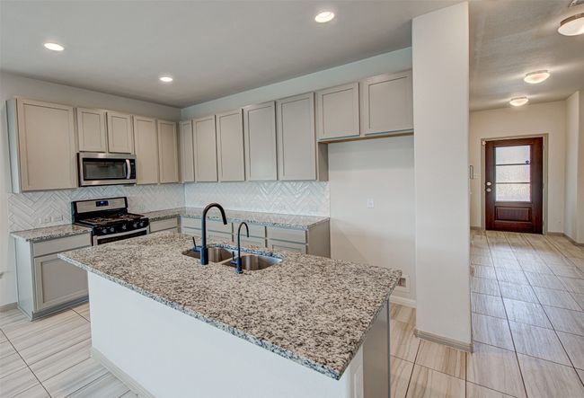 Kitchen with appliances with stainless steel finishes, a sink, light stone counters, gray cabinets, and backsplash | Image 10