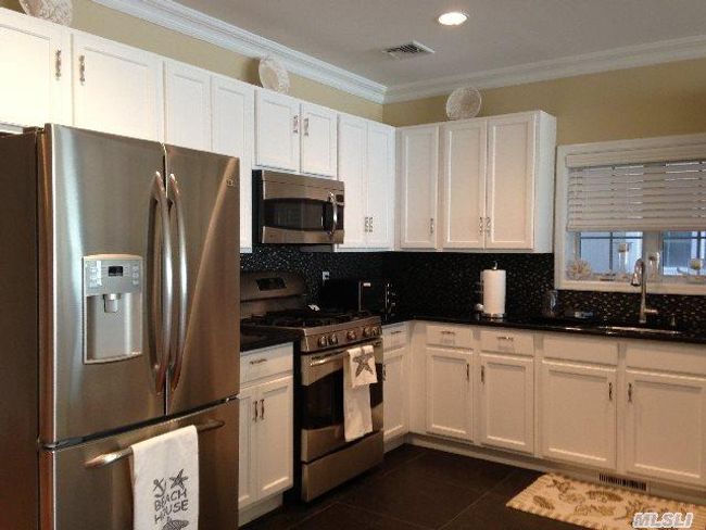 Kitchen featuring appliances with stainless steel finishes, dark tile patterned flooring, dark countertops, a sink, and white cabinets | Image 6