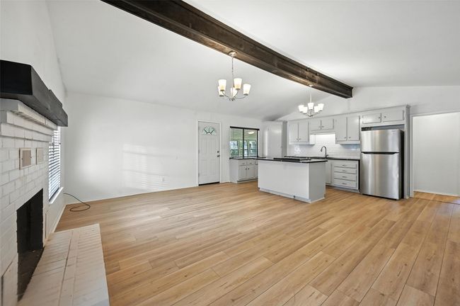 Kitchen with freestanding refrigerator, a chandelier, a fireplace, dark countertops, and light wood-type flooring | Image 5