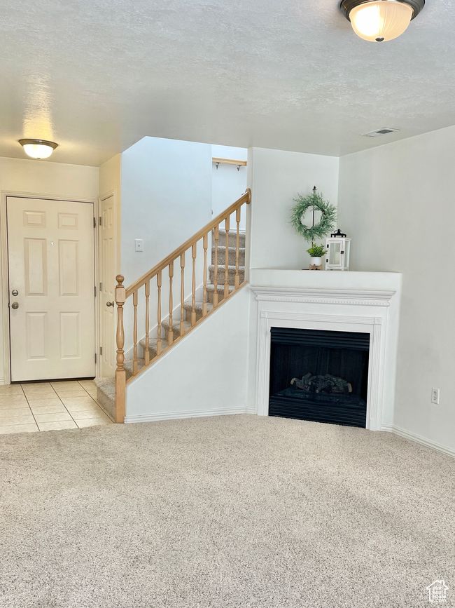 Unfurnished living room with carpet floors, a textured ceiling, stairs, a fireplace, and baseboards | Image 5