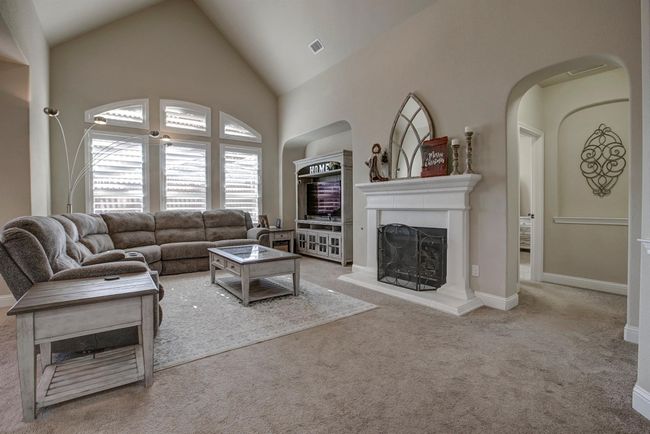 Carpeted living room with a fireplace with raised hearth, high vaulted ceiling, and arched walkways | Image 13