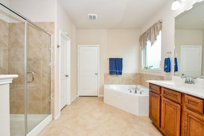 Spacious layout with a glass-enclosed shower, a large soaking tub, dual sinks with wooden cabinetry, and bright natural lighting from a window. | Image 18