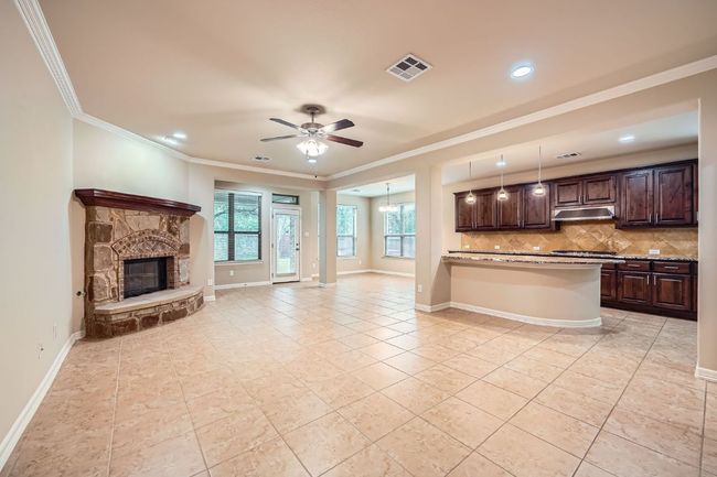 Kitchen with open floor plan, dark brown cabinets, crown molding, ceiling fan, and light tile patterned flooring | Image 6