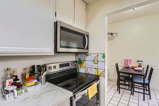 Kitchen featuring stainless steel appliances, light tile patterned flooring, tasteful backsplash, light stone counters, and white cabinetry | Image 14