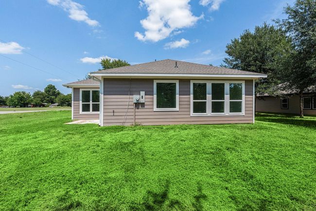 This photo shows the back view of a single-story home with a well-maintained lawn. The house features a neutral exterior and large windows, allowing for ample natural light. It is situated on a spacious corner lot with surrounding greenery and a clear blue sky overhead. | Image 43