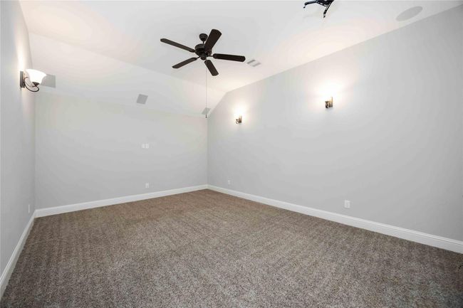 This bedroom features soft gray walls, plush carpet, and a ceiling fan. Wall-mounted lights provide a cozy ambiance, ideal for a media or a study. | Image 31
