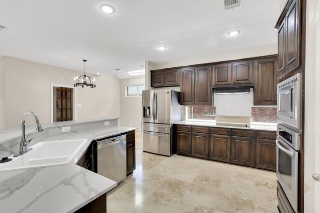 Kitchen with stainless steel appliances, a sink, visible vents, dark brown cabinetry, and a notable chandelier | Image 13