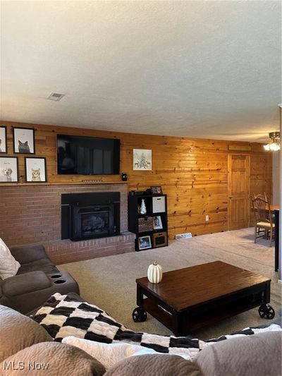 Carpeted living room featuring a fireplace, a textured ceiling, and wood walls | Image 2