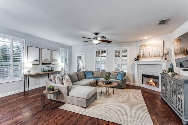 Living area with a glass covered fireplace, wood finished floors, ceiling fan, and healthy amount of natural light | Image 11