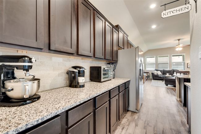 Kitchen with dark brown cabinets, appliances with stainless steel finishes, backsplash, light wood-type flooring, and lofted ceiling | Image 9