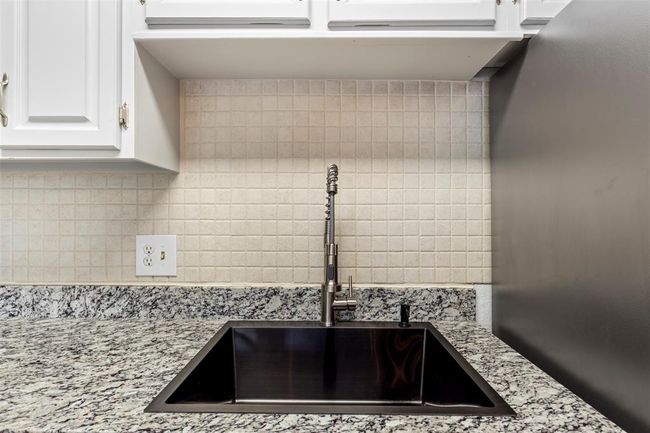 Kitchen view of tasteful backsplash, white cabinets, and light stone countertops | Image 13