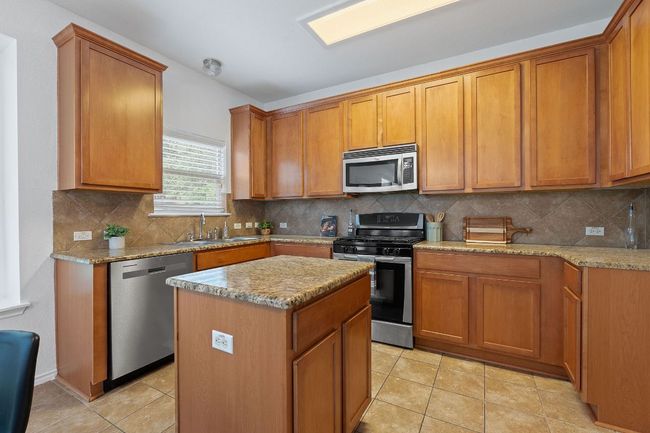 Kitchen featuring appliances with stainless steel finishes, a sink, a kitchen island, and light stone counters | Image 8