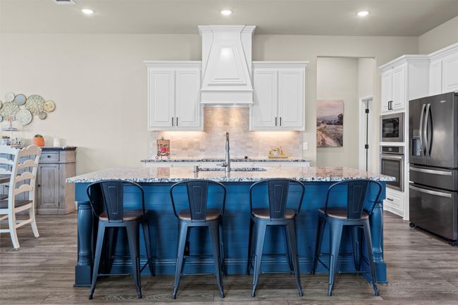 Kitchen featuring appliances with stainless steel finishes, premium range hood, light stone counters, a center island with sink, and white cabinetry | Image 5