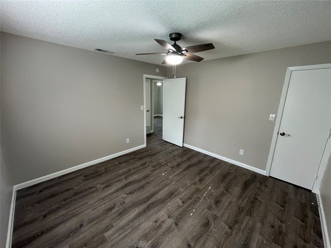 Unfurnished bedroom featuring dark wood finished floors, a textured ceiling, baseboards, and a ceiling fan | Image 13