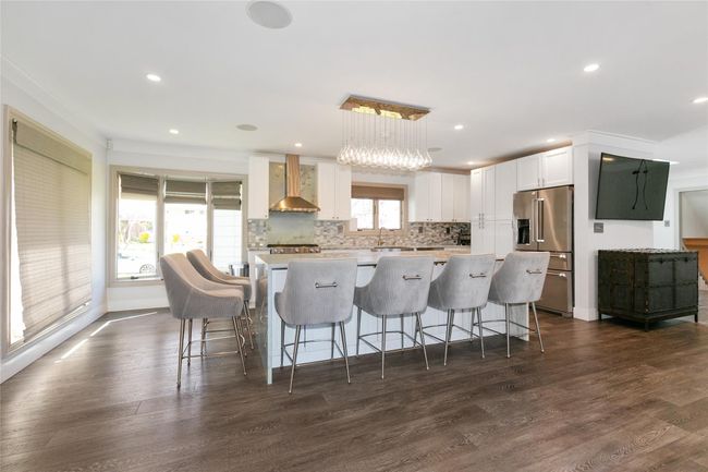 Kitchen with decorative backsplash, wall chimney range hood, white cabinets, high end refrigerator, and a center island | Image 7