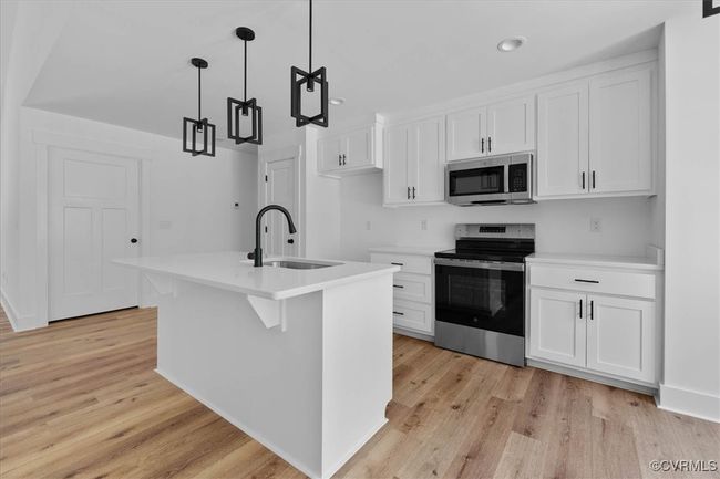 Kitchen featuring light wood-style floors, white cabinets, appliances with stainless steel finishes, and a sink | Image 13