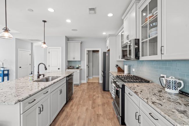 Kitchen with appliances with stainless steel finishes, decorative backsplash, light wood finished floors, white cabinetry, and glass insert cabinets | Image 8