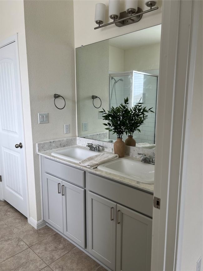 Spa-inspired Primary Bathroom with double vanity featuring trendy terrazzo-style quartz countertops, a glass-enclosed shower, and a freestanding soaking tub. | Image 10