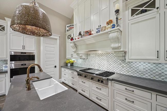 The kitchen is enhanced with under-counter lighting that beautifully highlights the quartz countertops. The upper cabinets feature glass panels, perfect for displaying fine china or decorative items, adding both style and functionality to the space. | Image 8
