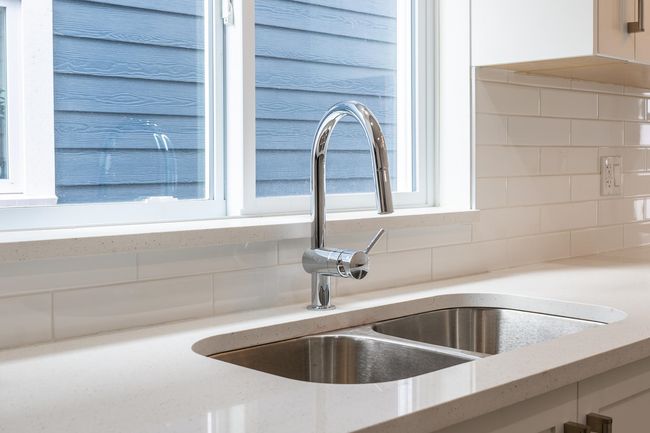 Kitchen view of a sink, backsplash, white cabinetry, and light stone countertops | Image 12