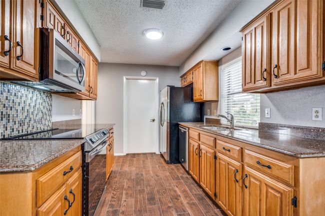 Kitchen with stainless steel appliances, a textured ceiling, dark wood-style floors, dark stone countertops, and tasteful backsplash | Image 13