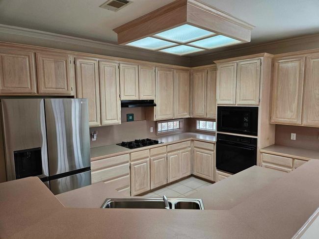 Kitchen featuring black appliances, light brown cabinetry, under cabinet range hood, light countertops, and ornamental molding | Image 20