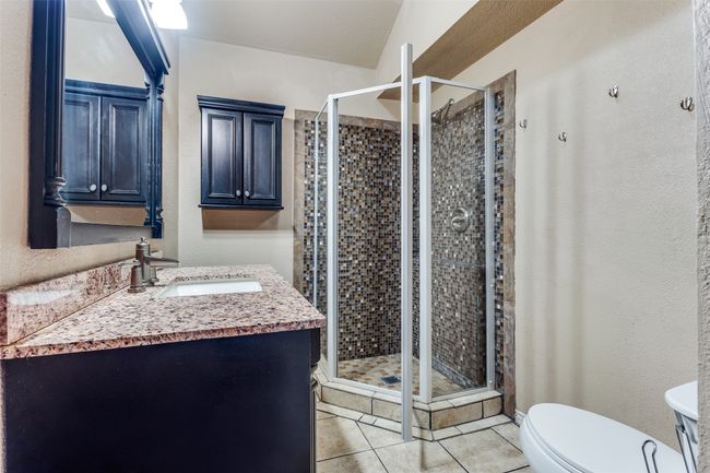 Bathroom featuring toilet, a stall shower, a textured wall, tile patterned floors, and vanity | Image 20