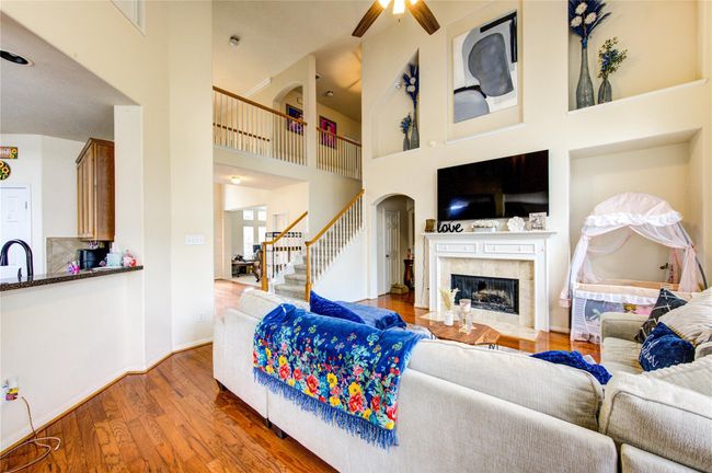 This spacious living room features high ceilings, a cozy fireplace, and an open floor plan. A large sectional sofa provides ample seating, while natural light floods the room. The elegant staircase leads to a second-floor balcony, adding to the airy feel. | Image 19