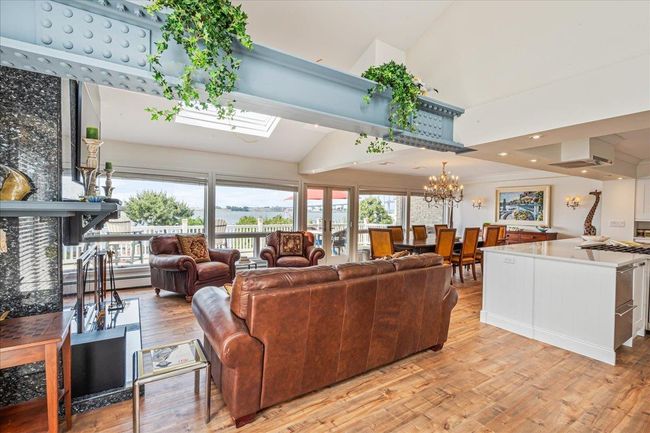Living area with light wood-style floors, high vaulted ceiling, a chandelier, baseboard heating, and a skylight | Image 5