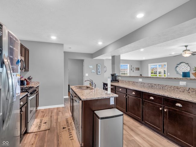 kitchen featuring a sink, light wood-type flooring, a center island with sink, light stone counters, and appliances with stainless steel finishes | Image 6