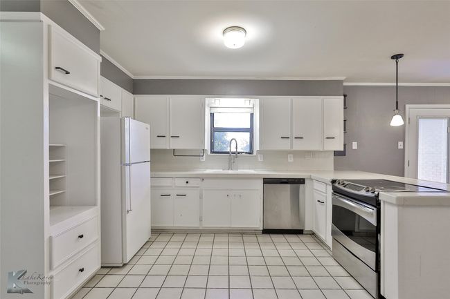Kitchen featuring appliances with stainless steel finishes, crown molding, sink, decorative light fixtures, and white cabinets | Image 4