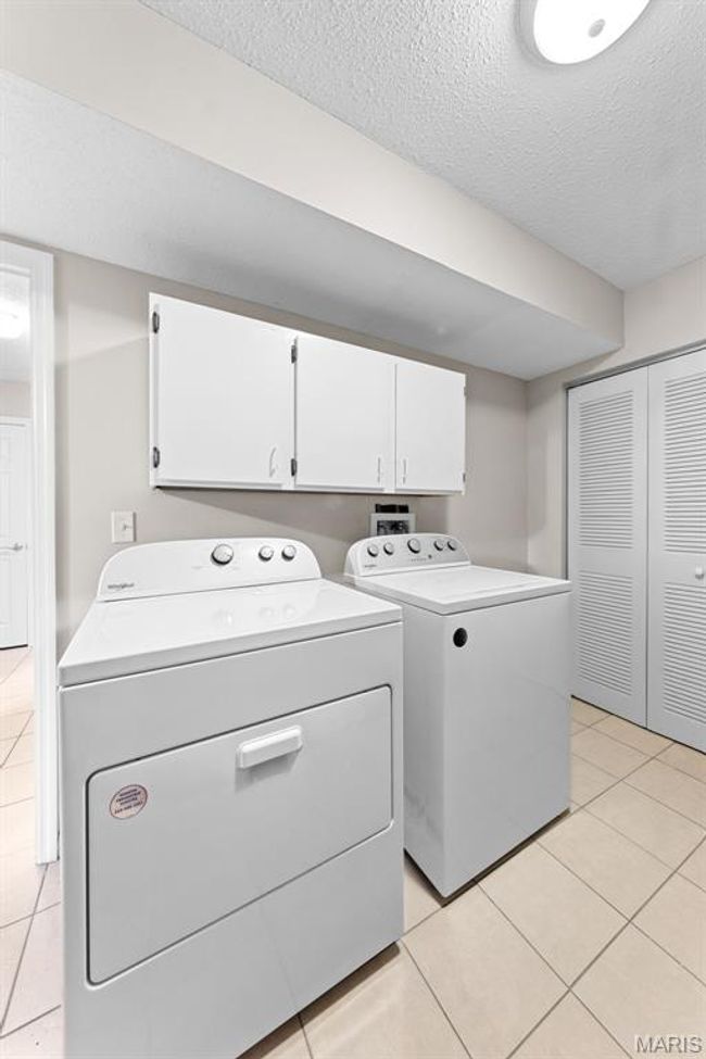 Private main floor laundry featuring cabinet space, washer and dryer included , and light tile flooring. | Image 21