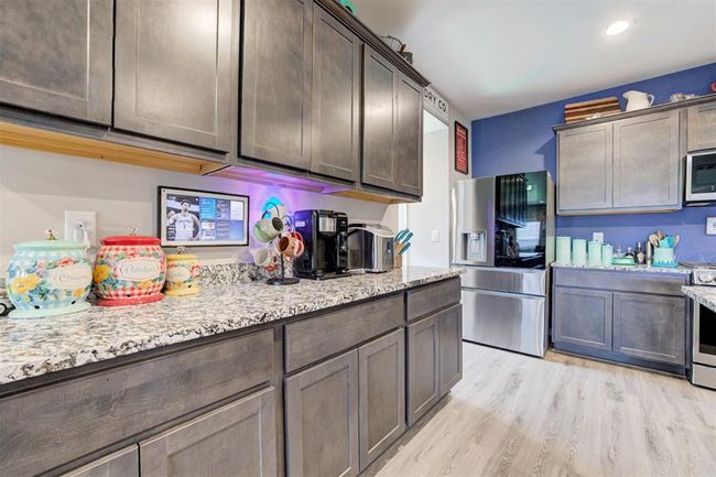 Kitchen featuring stainless steel appliances, light stone counters, dark brown cabinetry, light wood finished floors, and recessed lighting | Image 14