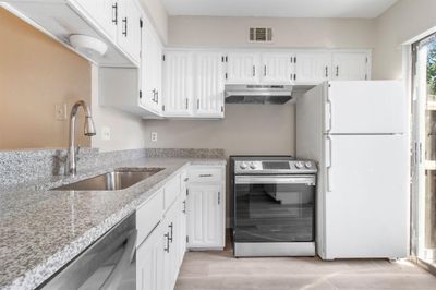 Kitchen featuring light hardwood / wood-style floors, sink, ventilation hood, white cabinets, and appliances with stainless steel finishes | Image 1